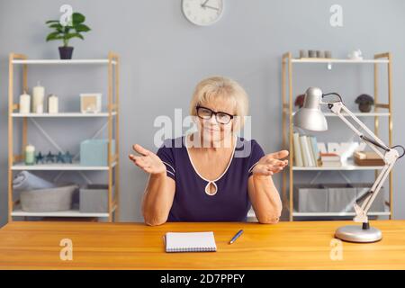 Donna anziana felice in occhiali seduti alla scrivania con blocco note, parlando e ascoltando con attenzione Foto Stock