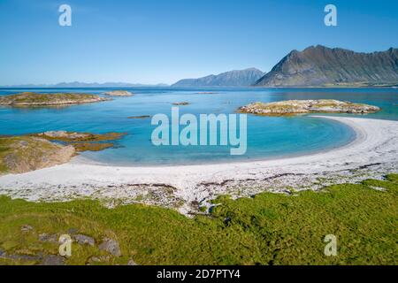 Baia a forma di mezzaluna, spiaggia di sabbia bianca, mare turchese, costa erbosa di fronte, ripide montagne dietro, Vagan, Lofoten, Nordland, Norvegia Foto Stock