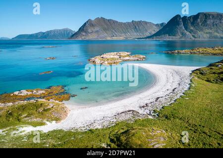 Baia a forma di mezzaluna, spiaggia di sabbia bianca, mare turchese, costa erbosa di fronte, ripide montagne dietro, Vagan, Lofoten, Nordland, Norvegia Foto Stock