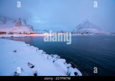 Atmosfera invernale sul fiordo, mattina presto nel villaggio di pescatori, nevicate in montagna, Reine, Nordland, Lofoten, Norvegia Foto Stock