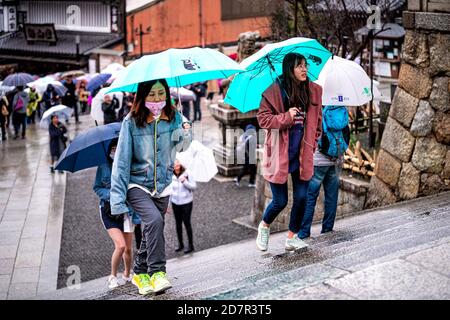 Kyoto, Giappone - 10 aprile 2019: Molte persone con ombrelloni salendo scale in maschera durante il giorno piovoso per strada vicino al tempio Kiyomizu-dera Foto Stock