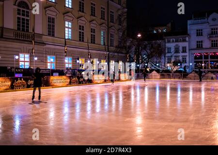 Lviv, Ucraina - 27 dicembre 2019: Piazza del mercato della città vecchia con pista di pattinaggio notturno a Lvov, luci di illuminazione natalizia e persone che pattinano Foto Stock