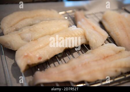 Filetti bianchi di merluzzo selvatico su una rastrelliera metallica che asciuga. Il pesce crudo viene preparato in una cucina del ristorante. Foto Stock