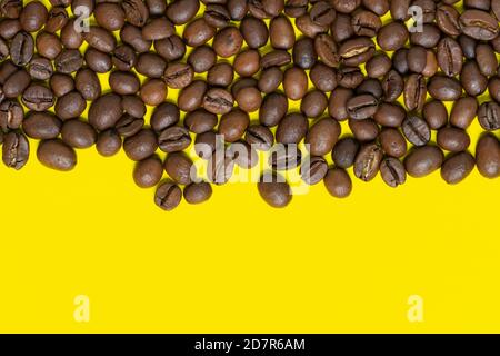 Chicchi di caffè marroni su sfondo giallo chiaro. Oggetti di posizione orizzontale superiore, copiare lo spazio per il testo in basso. Caffè piatto e da primo piano ancora vivo Foto Stock