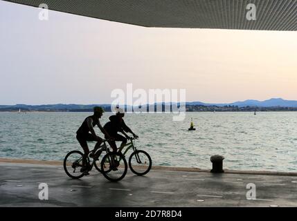 Ciclisti che percorrono il Paseo Maritimo de Santander Cantabria Spagna In una soleggiata mattina di ottobre all'ombra del Centro artistico Botin Foto Stock