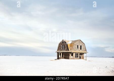 Una grande casa in stile fienile in buona forma abbandonato in un campo innevato in un paesaggio di campagna pomeridiana Foto Stock