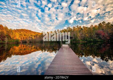 Molo in legno sul lago denso in autunno con riflessi nuvoloso - Foresta ricreativa di DuPont state - vicino a Cedar Mountain, North Carolina, USA Foto Stock