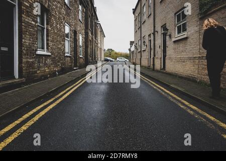 Vuota strada a senso unico vista in una città inglese. Due linee gialle si possono vedere su entrambi i lati, con una persona vista camminare sulla destra. Foto Stock