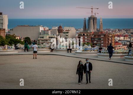 La Sagrada Familia appare sullo sfondo, mentre i visitatori che indossano maschere a piedi la spianata di Piazza della natura del Parco Guell di Barcellona. La Spagna si avvicina ad un altro stato di allarme dopo che otto regioni hanno invitato il governo ad attuare la misura di emergenza per contrastare le infezioni da coronavirus. Foto Stock