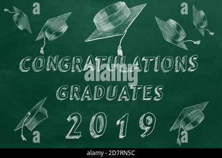 Testo di disegno a mano 'Congratulazioni laureati. 2019.' e tappi graduati sulla lavagna verde. Foto Stock