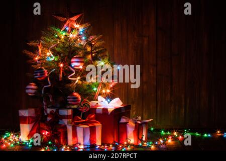 Decorato albero di Natale illuminato e scatole regalo su sfondo di legno Foto Stock