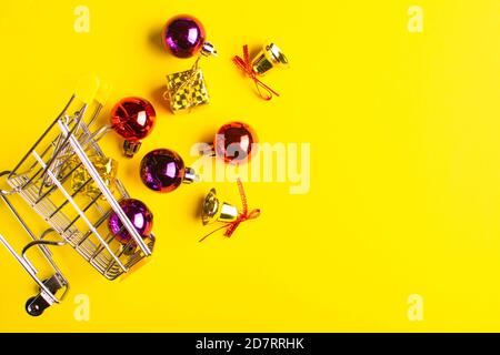 Carrello pieno di palle di natale, regali e campane scintillanti su sfondo giallo. Foto Stock