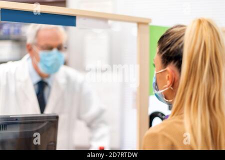 Farmacista utile che indossa una maschera di coronavirus covid che parla con a. cliente Foto Stock