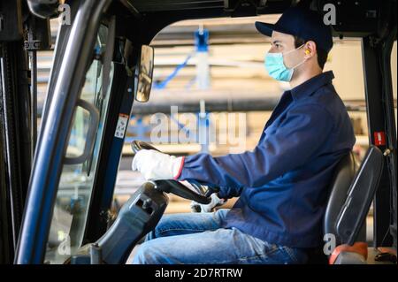 Un bel lavoratore di costruzione che guida un carrello elevatore in un impianto industriale Foto Stock