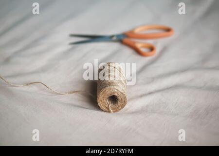 Sul morbido tessuto leggero si trova una bobina di corda di canapa grossolana e moderne forbici affilate. Cucito e hobby. Foto Stock