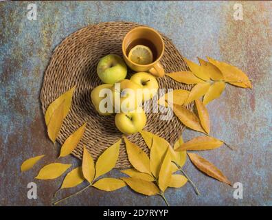 Ancora vita di mele dorate e infusione calda in tazza gialla, su fondo blu Foto Stock