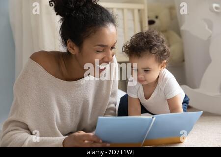 Sorridente mamma biraciale leggere il libro con bambino neonato Foto Stock