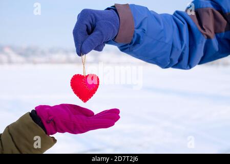 Un uomo dà un cuore sentito ad una donna il giorno di San Valentino. Cuore di San Valentino in mani maschili e femminili. Foto Stock
