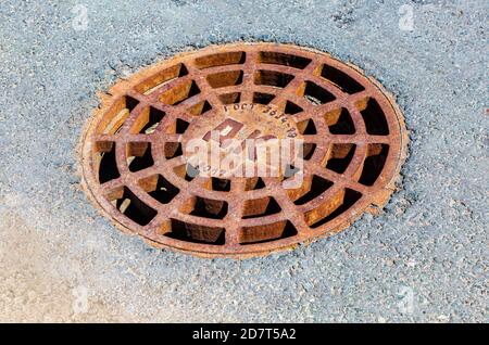 Copertura di tombino in metallo arrugginito su strada asfaltata urbana. Tondino fognario di drenaggio Foto Stock