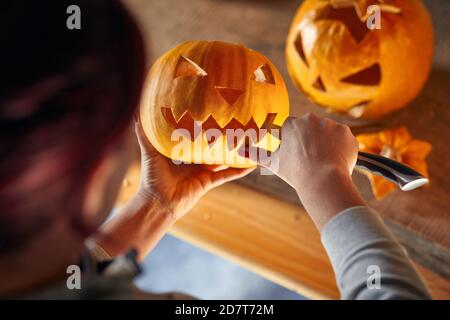 Donna che intagliava la zucca di Halloween a casa; la zucca di Halloween con una faccia scolpita Foto Stock