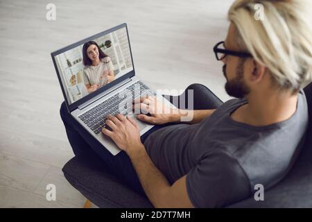 Il giovane freelancer è a casa, si siede in una sedia e comunica online con una donna. Foto Stock