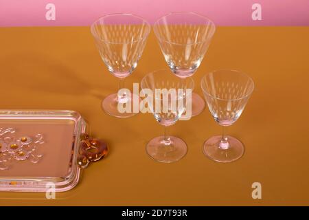 Set di eleganti bicchieri da cocktail martini in piedi accanto a un piatto da portata di vetro su una superficie marrone e uno sfondo rosa. Pulito minimalista ed elegante Foto Stock