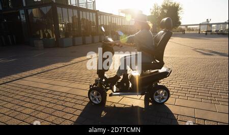 Donna turistica in sella a uno scooter elettrico a quattro ruote su una strada cittadina. Foto Stock