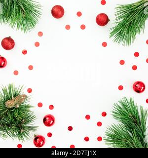 Cornice natalizia in rami di pino e palline rosse con confetti su bianco. Disposizione piatta, vista dall'alto Foto Stock