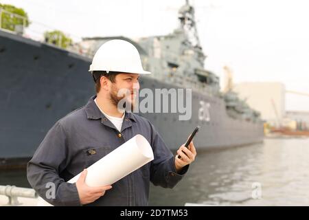 Ingegnere marino che parla da VHF walkie talkie, tenendo carte vicino nave in background. Foto Stock