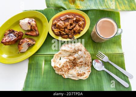 Vista panoramica di roti canai o paratha servito su foglie di banana, con curry di montone e pollo fritto Foto Stock