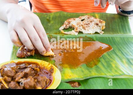 Persona che si gode mangiare roti canai servito con curry su banana foglia con la mano Foto Stock