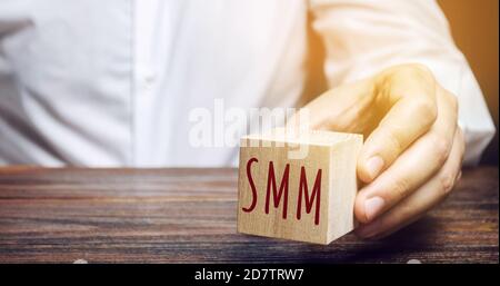 Uomo d'affari che tiene un blocco di legno con la parola SMM. Concetto di Marketing sui social media. Promuovere un prodotto e un servizio. E-marketing, marketing digitale. IO Foto Stock