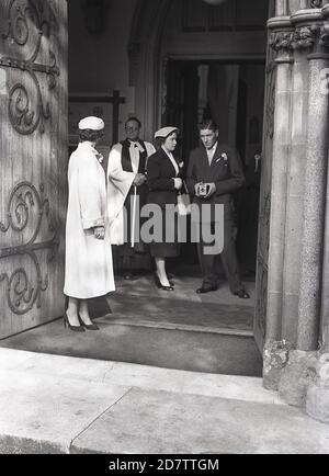 1950, storico, all'ingresso di una chiesa tre ospiti di nozze e il sacerdote, con l'uomo che ha in mano una macchina fotografica Kodak 'Brownie' box film. Foto Stock