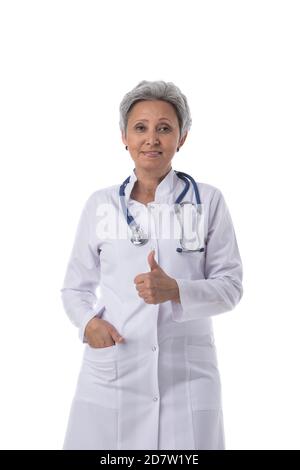 Asian maturo medico femminile con stetoscopio isolato su sfondo bianco, pollice su gesto Foto Stock
