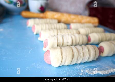 Sbozzati per torte fritte. Le salsicce sono avvolte in sottili strisce di impasto di lievito. L'impasto si sta alzando. Messa a fuoco selettiva Foto Stock