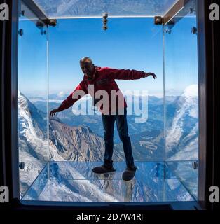 Tourist si trova nella scatola di vetro 'SUP into the Void' sull'Aiguille Du Midi (3842m) in cima alla montagna Chamonix Mont-Blanc, Francia. Foto Stock