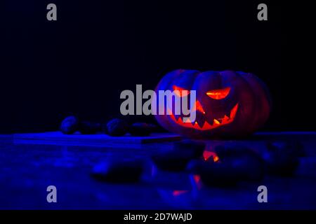 Zucca di Halloween con alcuni muffin di zucca fuori fuoco in primo piano e più muffin su una tavola di legno accanto ad essa, il tutto su uno sfondo scuro. Foto Stock