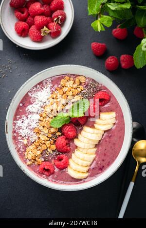 Recipiente per frullato di lamponi vegano con guarnizioni superfood su fondo nero in cemento, vista dall'alto Foto Stock