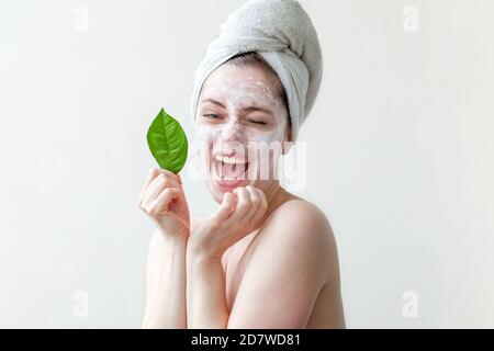 Bellezza minima ritratto donna ragazza in asciugamano sulla testa applicando maschera nutriente bianca o crema sul viso, foglia verde in mano isolato sfondo bianco. Pulizia della pelle eco biologico cosmetico concetto spa Foto Stock