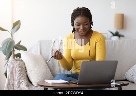 Millennial African Lady in Headset Watching Webinar online su laptop A casa Foto Stock