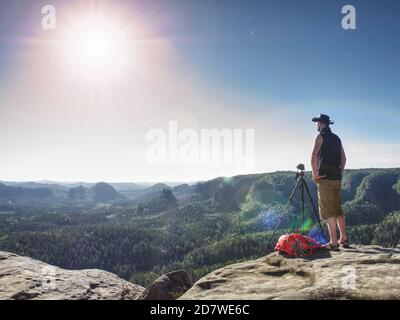 Cowboy escursionista a macchina fotografica su treppiede, guardando nel paesaggio e pensare. L'uomo con cappello da cowboy in pelle ascolta il suono della natura pura. Foto Stock