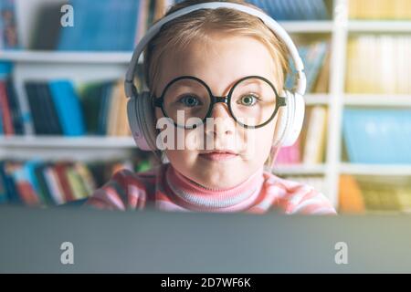 Bambina intelligente che indossa grandi occhiali mentre usa il suo computer portatile. Foto di alta qualità Foto Stock