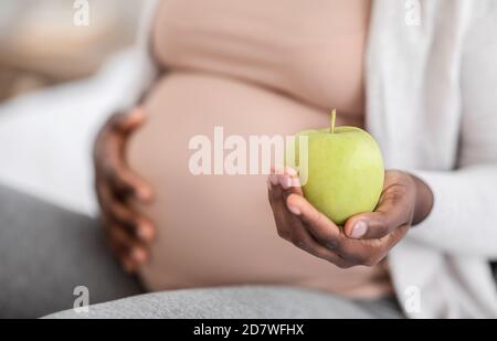 Donna incinta nera che tiene la mela verde organica, godendo di nutrizione sana durante la gravidanza Foto Stock