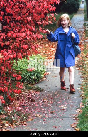 Giovane studentessa rossa cammina attraverso le foglie cadute nel nord-est degli Stati Uniti 1990 Foto Stock