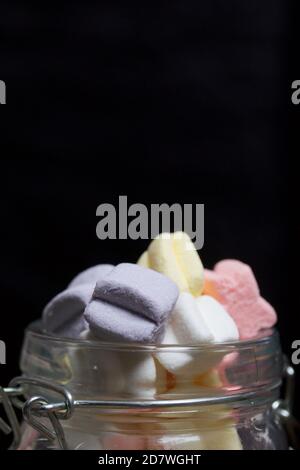 Marshmallows di colori diversi. Giacciono in vaso di vetro. Primo piano fotografato su sfondo nero. Foto Stock