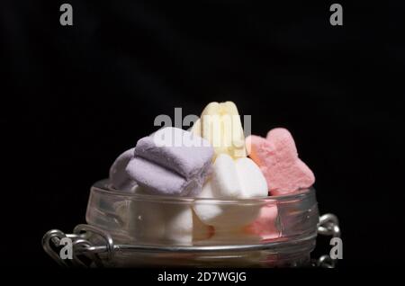 Marshmallows di colori diversi. Giacciono in vaso di vetro. Primo piano fotografato su sfondo nero. Foto Stock
