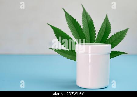Foglia di cannabis e confezione di plastica o barattolo con copia spazio con olio di canapa contenente crema Foto Stock