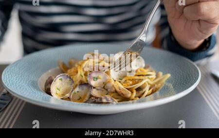 Dettaglio mano maschile mangiare spaghetti di pasta con vongole e triglie, cucina mediterranea