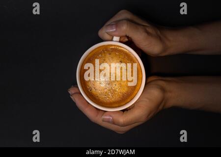 Tazza bianca di caffè con crema in mano. Vista dall'alto Foto Stock