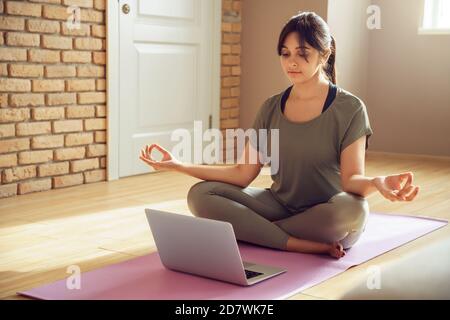 Giovane calma donna indiana meditare guardando online lezione di yoga a casa. Foto Stock